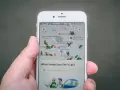 Una mano sostiene un teléfono mostrando una aplicación de localización móvil con un mapa lleno de iconos de insectos verdes y varios puntos de interés.