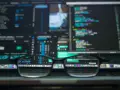 Gafas reflejan código y software de edición, mostrando la complejidad de **malware vs virus** en la era digital.