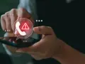 Mano sosteniendo un teléfono con un icono de llamada y advertencia.