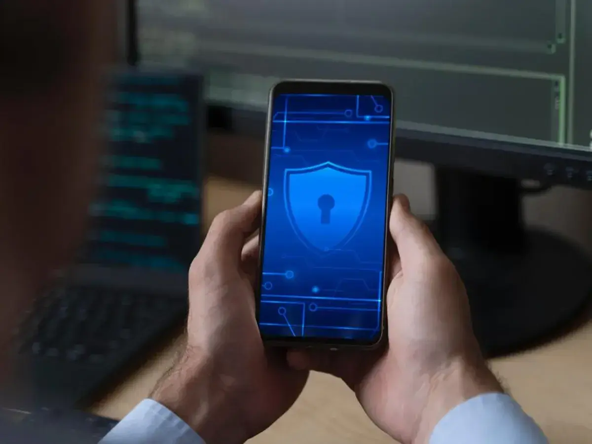 Man holds phone with shield icon, hinting at security concerns like Pegasus.