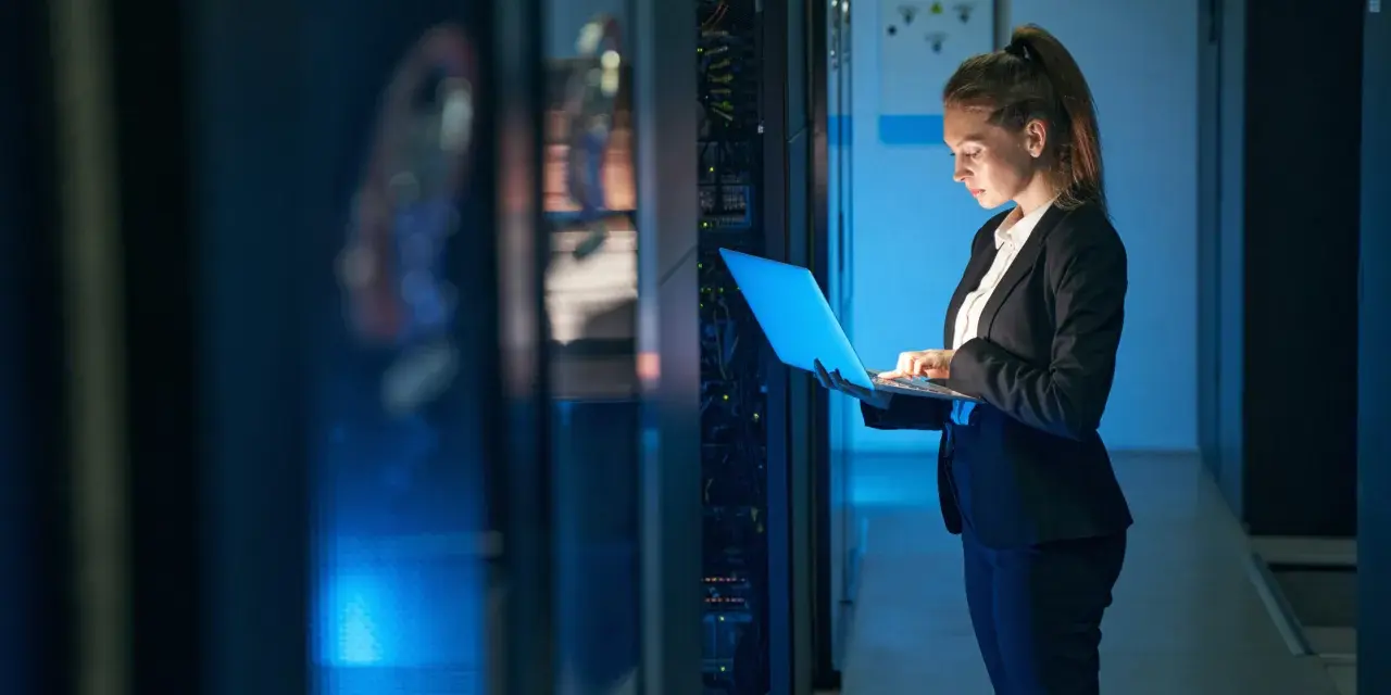 Mujer con portátil en centro de datos, gestionando infraestructura como servicio (IaaS) y soluciones SOC as a service.