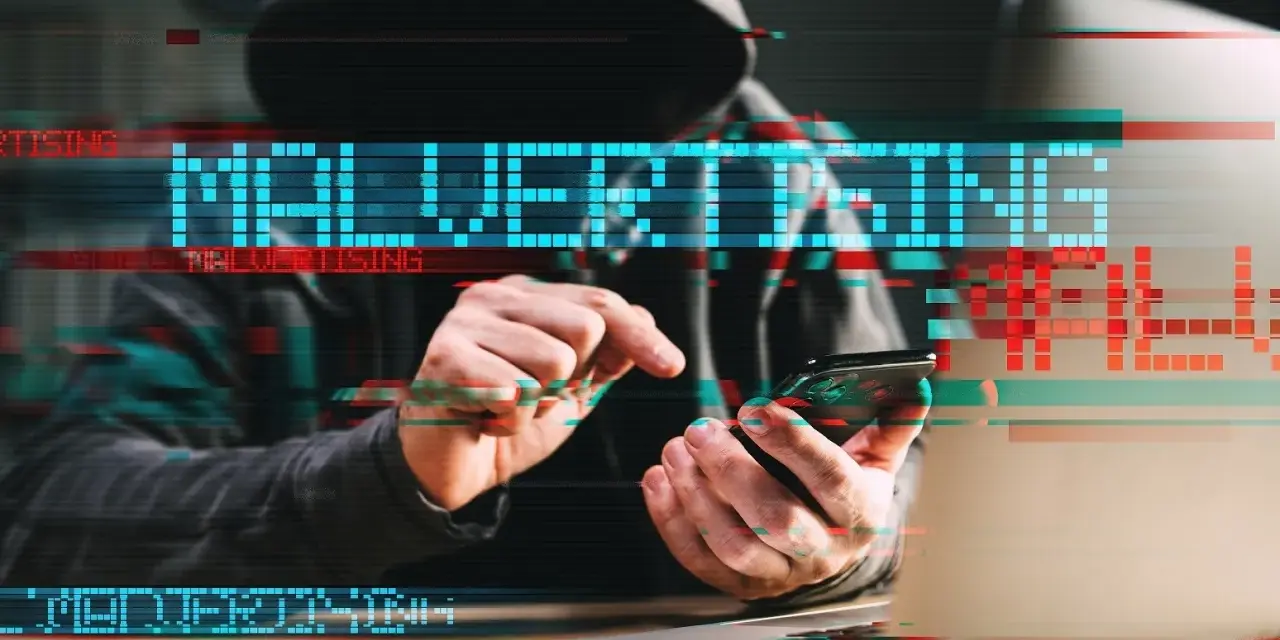 Persona con capucha usa un teléfono, con el texto "MALVERTISING" superpuesto, ilustrando qué es el malvertising.