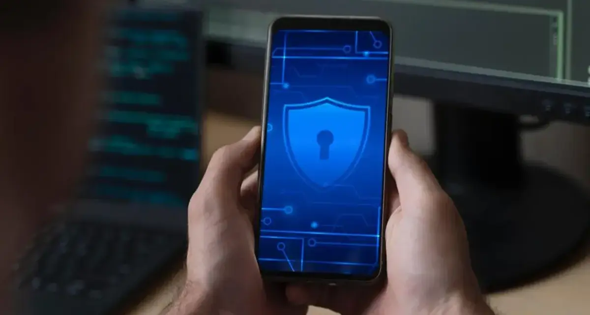 Man holds phone with shield icon, hinting at security concerns like Pegasus.