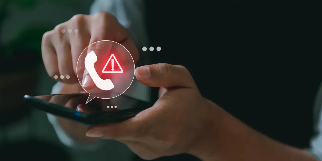 Mano sosteniendo un teléfono con un icono de llamada y advertencia.