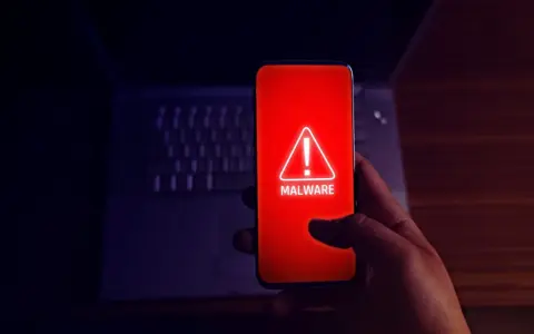 Alerta en el móvil: el teléfono muestra un aviso de "MALWARE" en rojo, indicando el peligro de apps maliciosas.