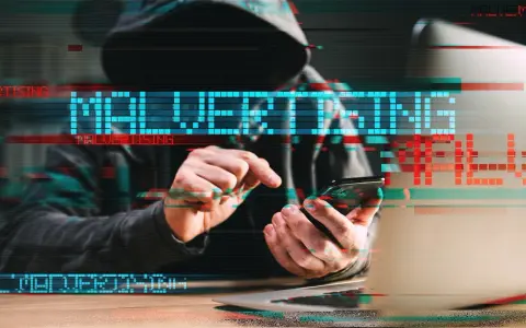 Persona con capucha usa un teléfono, con el texto "MALVERTISING" superpuesto, ilustrando qué es el malvertising.