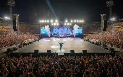 Artista en un estadio ante miles de fans. La multitud levanta sus teléfonos, como si quisieran saber **como ver ubicación en tiempo real** de sus amigos en el concierto.