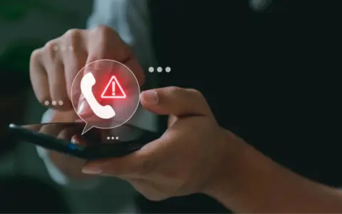 Mano con móvil, icono de llamada con advertencia. ¿Por qué recibo tantas llamadas spam?