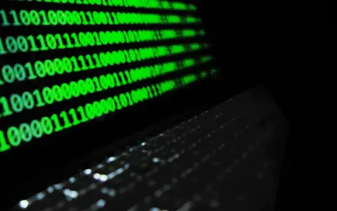 Código binario verde en pantalla, reflejando un teclado. ¿Qué es idp.generic? Es la base de la información digital.