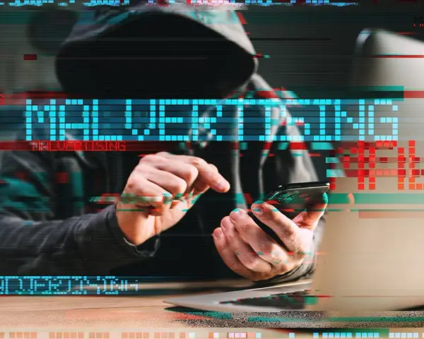 Persona con capucha usa un teléfono, con el texto "MALVERTISING" superpuesto, ilustrando qué es el malvertising.