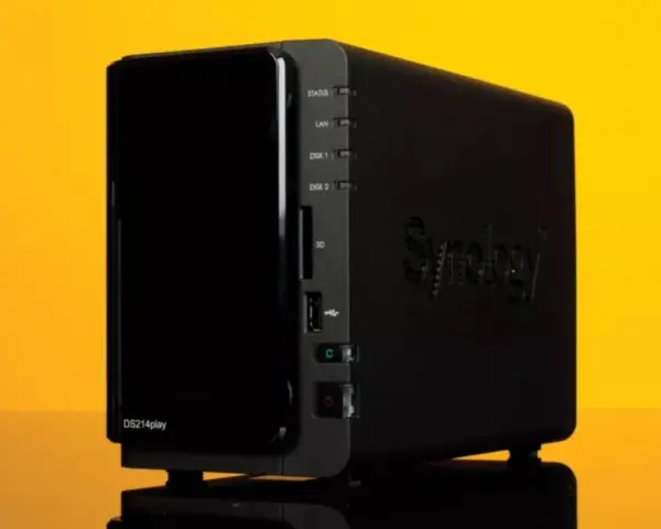 Servidor NAS Synology DS214play negro con luces indicadoras y logo en relieve, sobre fondo amarillo.