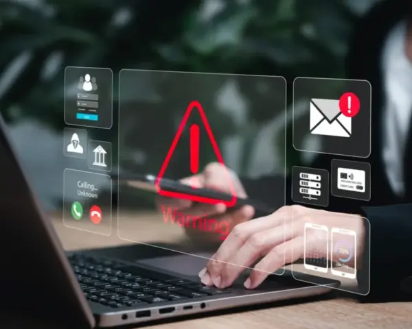 Alerta de seguridad digital: un mensaje falso podría estar acechando. Iconos de advertencia, correo, tarjetas y teléfonos flotan sobre un portátil.