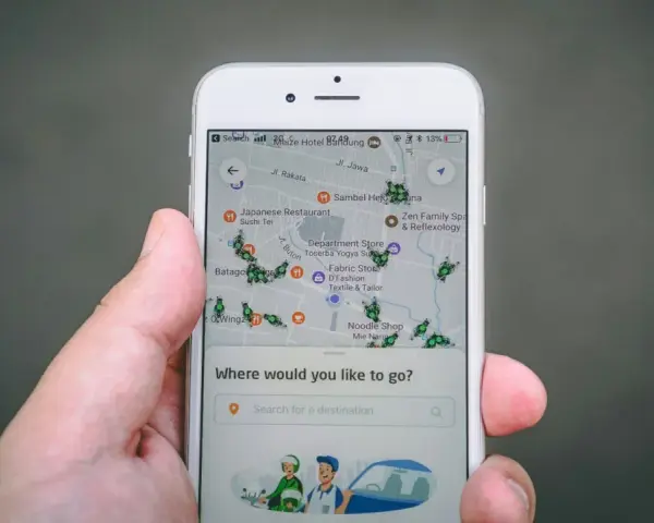 Una mano sostiene un teléfono mostrando una aplicación de localización móvil con un mapa lleno de iconos de insectos verdes y varios puntos de interés.