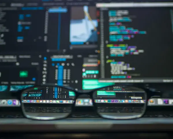 Gafas reflejan código y software de edición, mostrando la complejidad de **malware vs virus** en la era digital.