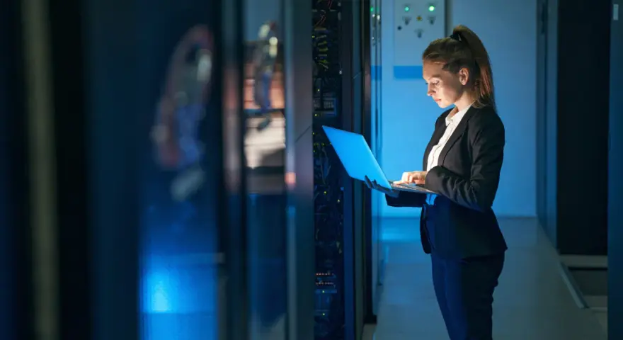 Mujer con portátil en centro de datos, gestionando infraestructura como servicio (IaaS) y soluciones SOC as a service.