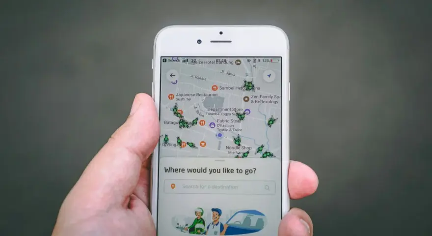 Una mano sostiene un teléfono mostrando una aplicación de localización móvil con un mapa lleno de iconos de insectos verdes y varios puntos de interés.