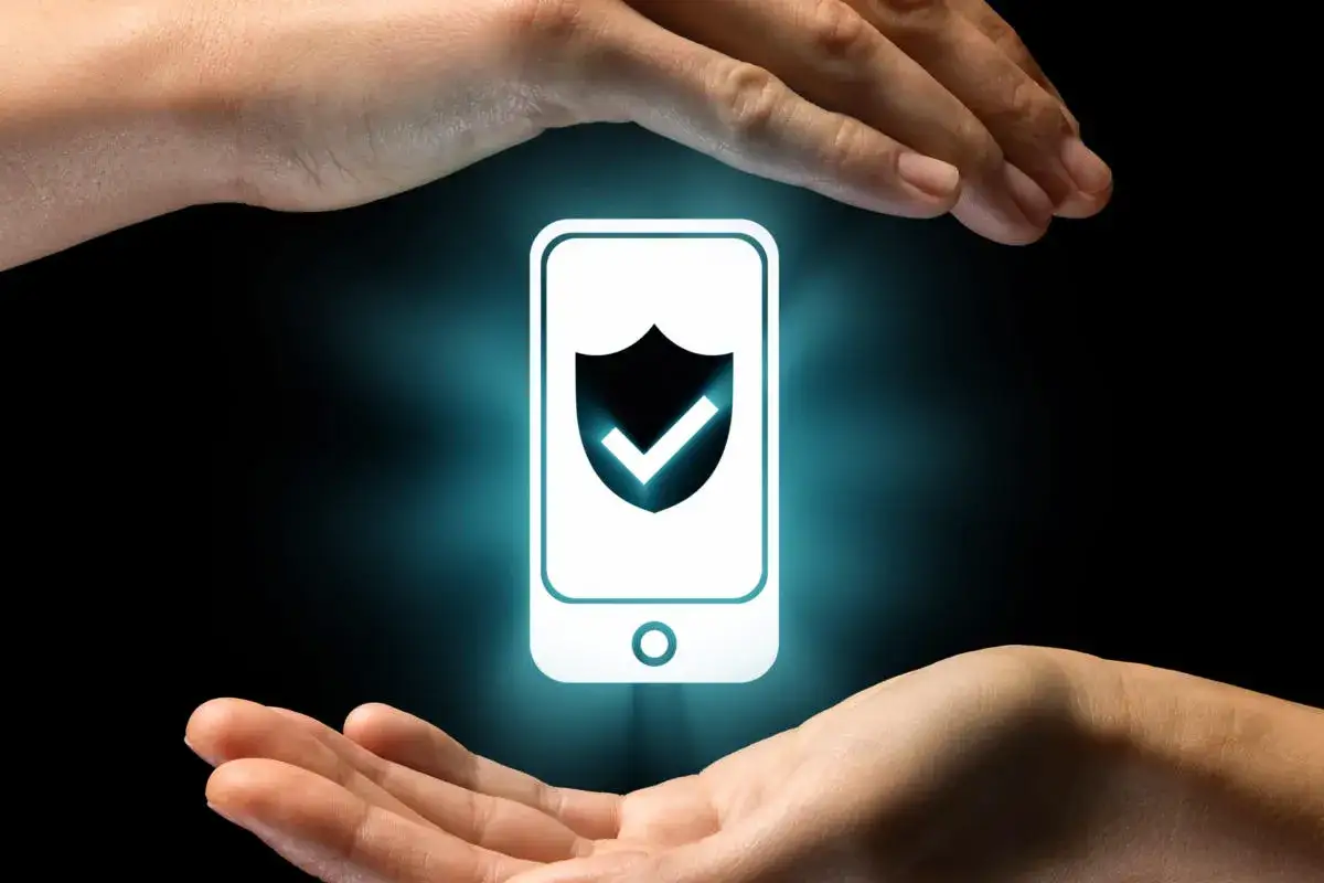 Manos protegen un m&oacute;vil con un escudo de seguridad. Aprende como saber si me han hackeado el m&oacute;vil.