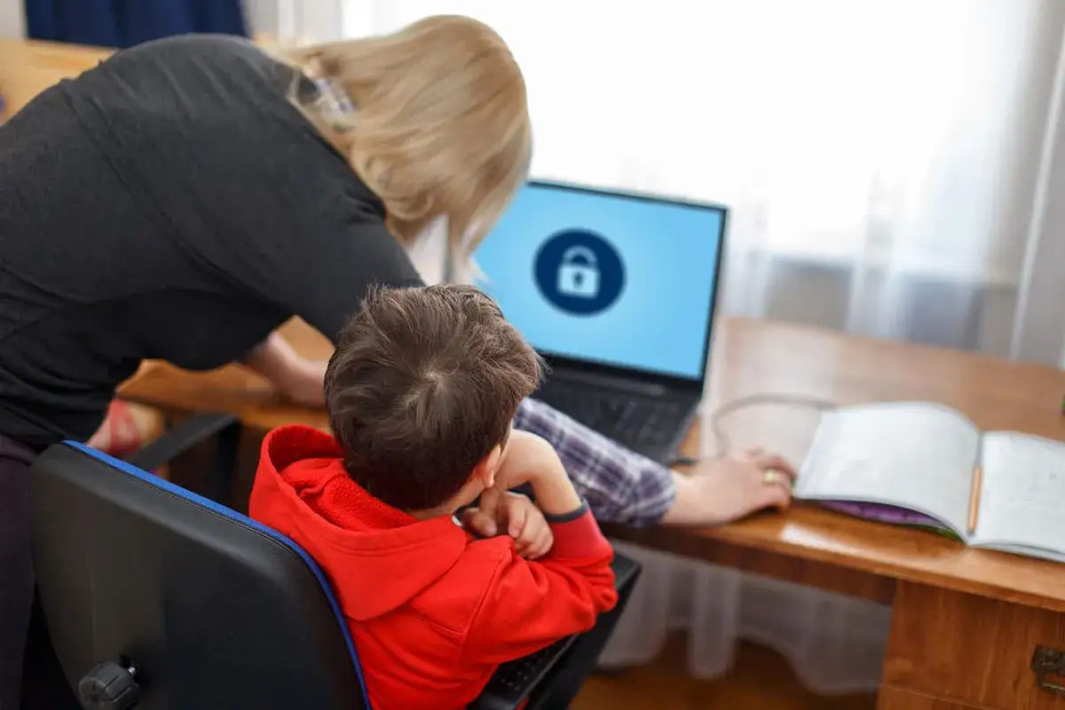 Madre ayuda a su hijo a configurar un app para limitar uso móvil niños gratis, con un candado en la pantalla del portátil.