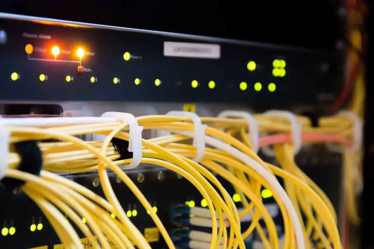 Detalle de un rack de servidores con luces de estado encendidas y un mont&oacute;n de cables de red amarillos organizados.