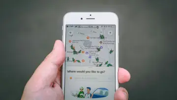 Una mano sostiene un teléfono mostrando una aplicación de localización móvil con un mapa lleno de iconos de insectos verdes y varios puntos de interés.