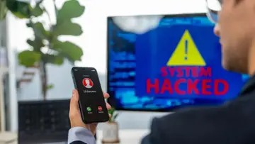 Un hombre recibe una llamada de un número desconocido mientras en la pantalla se lee "SYSTEM HACKED". ¡He sido hackeado!