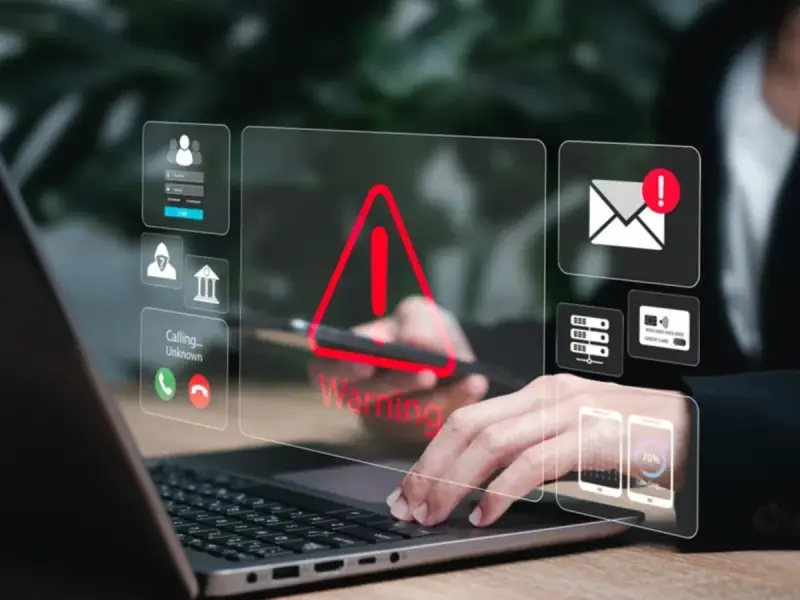 Alerta de seguridad digital: un mensaje falso podría estar acechando. Iconos de advertencia, correo, tarjetas y teléfonos flotan sobre un portátil.