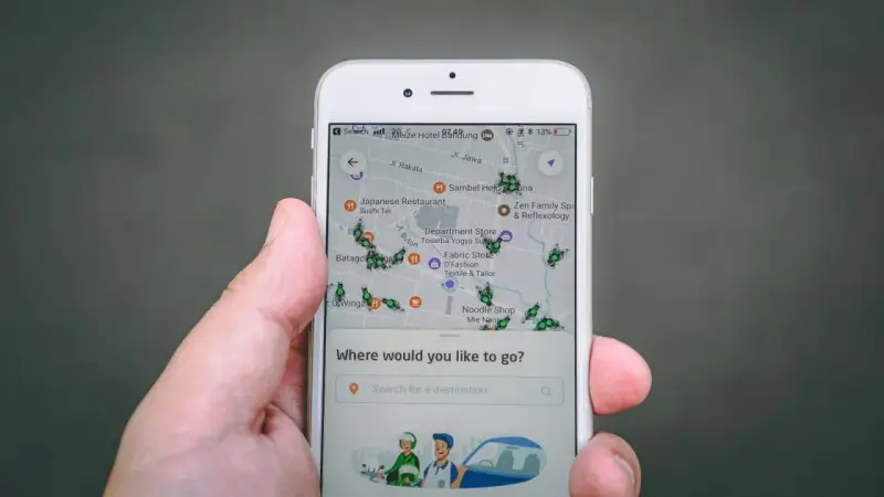 Una mano sostiene un teléfono mostrando una aplicación de localización móvil con un mapa lleno de iconos de insectos verdes y varios puntos de interés.